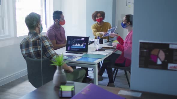 Diverse colleagues wearing face masks working together in meeting room at modern office