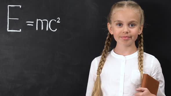 Smart Schoolgirl Pointing Chalk Into Physical Formula Written on Blackboard
