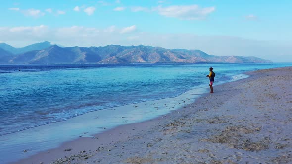 Single guy fishing alone on idyllic bay beach wildlife by aqua blue sea with white sandy background 