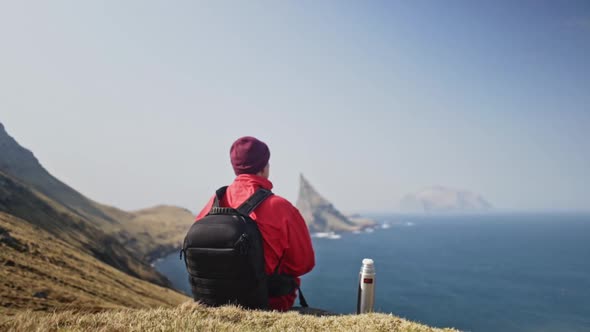 Man Sitting on Small Hill with Panoramic View of Ocean Waters in Faroe Islands