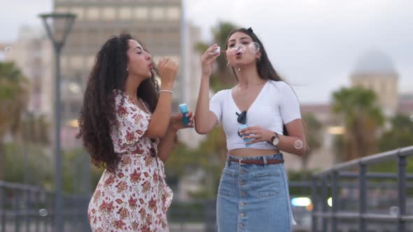 Young Multiethnic Hipster Women Having Fun Blowing Bubbles on Pier