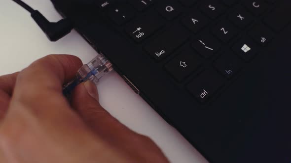 Close up of a male office worker plugging in a USB cable into a USB port on a black laptop