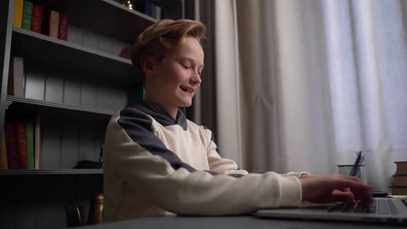 Closeup Side View of Joyful Crazy Child Boy Typing on Laptop Keyboard Sitting at Desk Near Window at