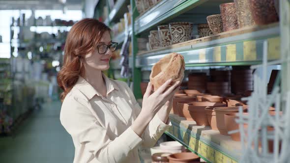 Young Beautiful Girl with Glasses for Vision Chooses Pots with Modern Design for Home Plants To