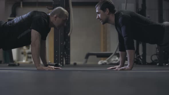 Side View of Adult Men Pushing Up in Gym. Young Healthy Caucasian Sportsmen Exercising in Fitness