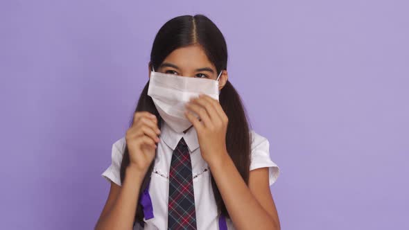 Funny Indian School Girl Putting Uncomfortable Face Mask on Violet Background