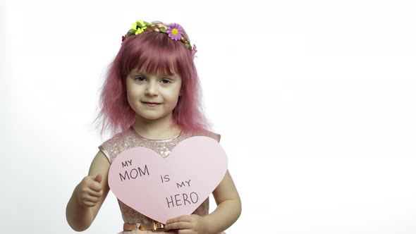 Child Girl Princess Holds Pink Paper Heart with Text About Mother. Mother's Day