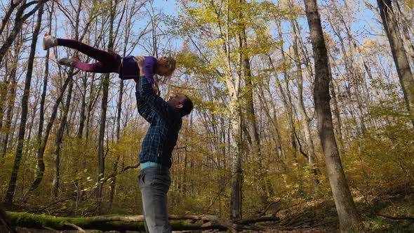 In slow motion, a father tosses his daughter while standing in an autumn forest