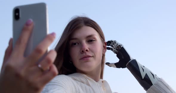 Portrait of a Young Woman with a Bionic Hand Who Takes a Selfie on a Smartphone