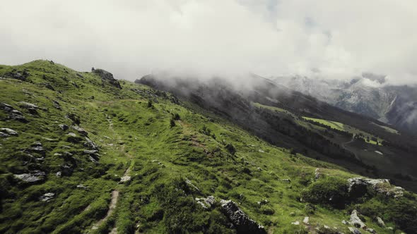 Aerial drone shot of a grass covered mountain top with a small trail leading along. More green mount