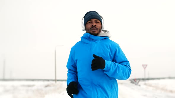 AfricanAmerican Man Wearing Headphones and Winter Clothes Trains Jogging Outdoors Front View