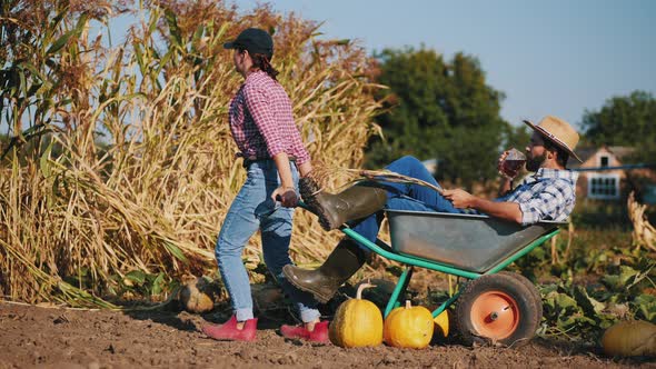 Woman Takes Away a Wheelbarrow with a Resting Farmer