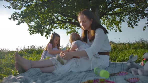 Young Mom Puts Sandals on Her Little One-year-old Daughter.