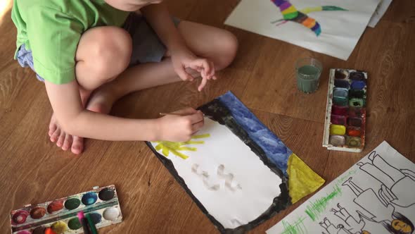 A Child on the Floor Draws a Drawing with Watercolors