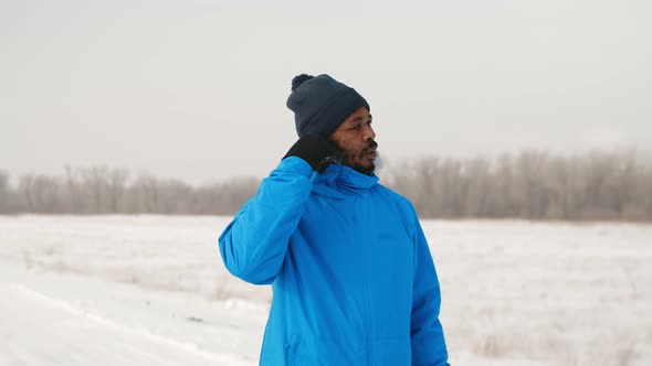 Black Man in Winter Clothes Inserts Headphones Into His Ears and Begins His Run Outdoor Front View