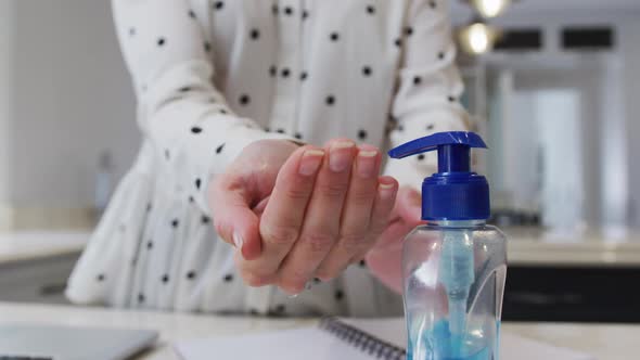 Mid section of woman sanitizing her hands at home