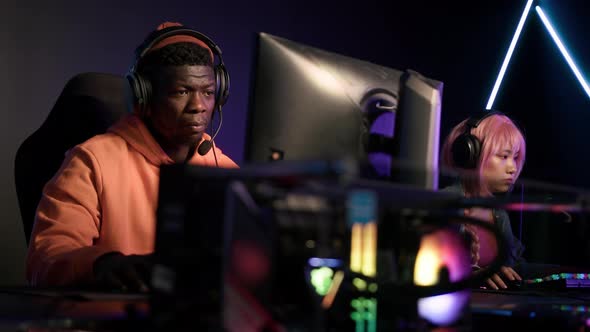 Cheerful AfricanAmerican in an Orange Hoodie Sitting in a Cyber Cafe Winning Another Match with His