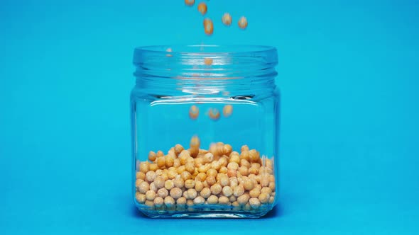 Closeup of Falling Down Chickpeas Into Glass Jar on Blue Background
