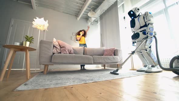 One Cyborg Uses Vacuum Cleaner While a Woman Talks on a Phone. Robot and Human Cooperation.