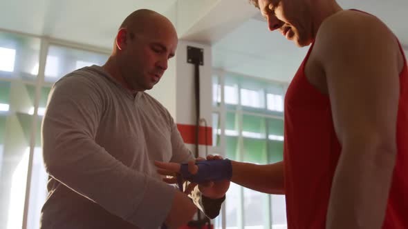 Caucasian man wrapping another man hands at gym