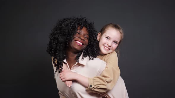 Afroamerican Lady with Curly Hair Holds Joyful Girl on Back