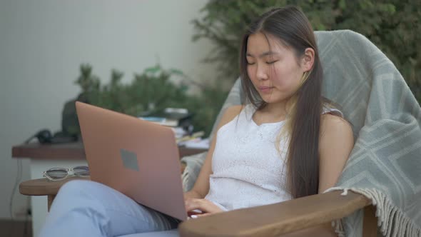 Concentrated Professional Asian Woman Typing on Laptop Keyboard Sitting in Home Office on Deck