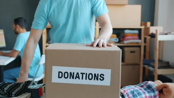 Closeup of Volunteer in Uniform Packing Donation Box Working in Charity Company