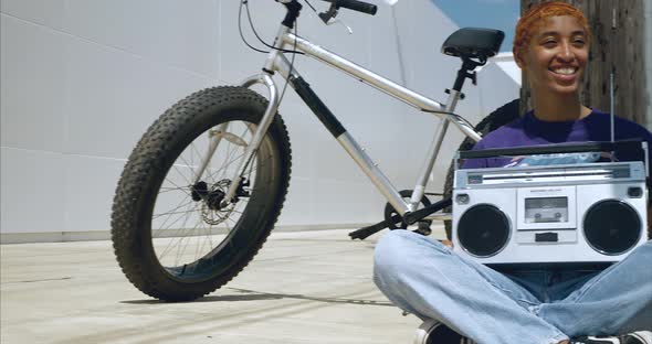 Panning shot of African American female holding boom box while sitting on ground