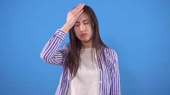 Young Asian Woman in a Shirt Makes Face Palm on a Blue Background