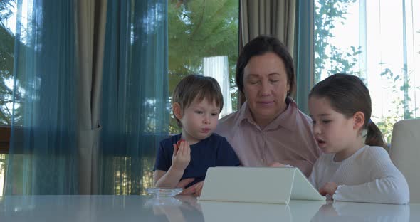 Grandma Entertaining Her Little Grandchildren with a Tablet Computer Game