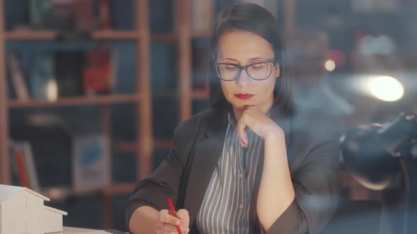 Pensive Female Architect Drawing Construction Plan at Desk in Office