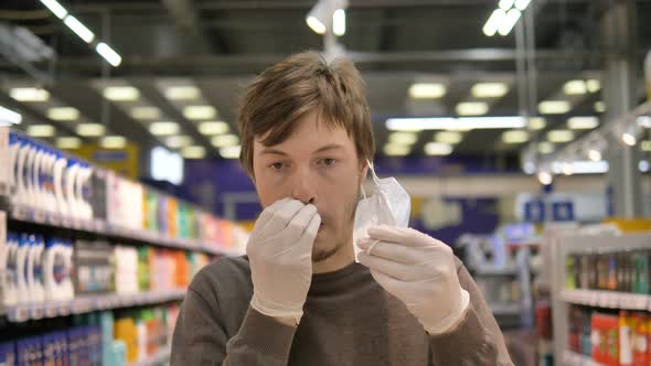 Man in a Medical Mask and Rubber Gloves in a Supermarket Removes the Mask and Scratches His Nose and