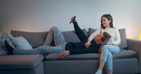 A Young Couple Watching TV, Resting, Hugging, Relaxing. Handsome Man and Attractive Woman Sitting on