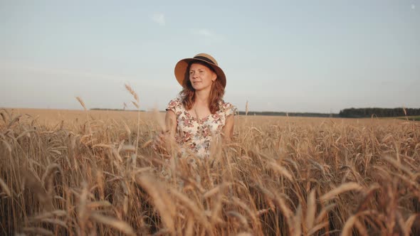 A Tender Young Woman Stands in a Wheat Field and Looks to the Sky Putting your Hand Over the Hat