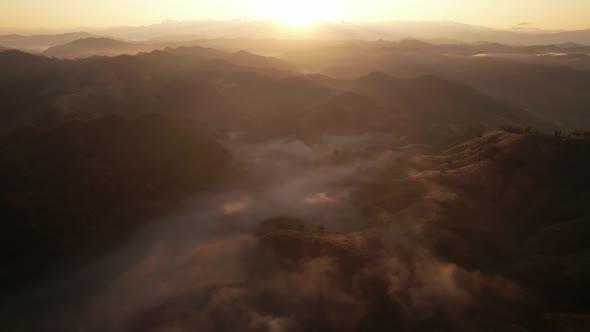 Aerial view of sunrise with fog above mountains. Golden hour and amazing sun rays. Nan, Thailand