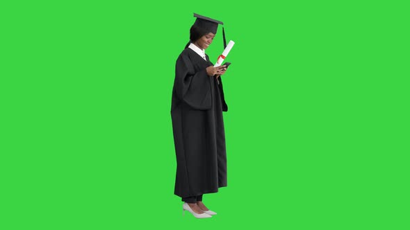 Happy African American Female Graduate Holding Diploma and Texting on Her Phone on a Green Screen