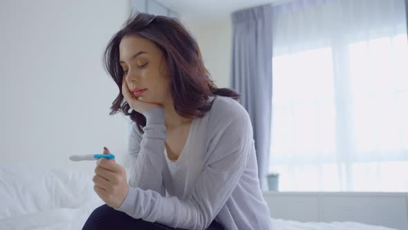 Asian disappointed young unplanned woman feeling shock after look at positive Pregnancy test.