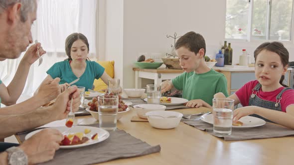 Three kids having breakfast of pancakes and fruits with their parents