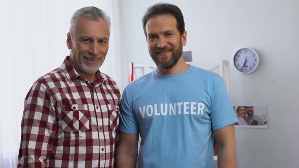 Middle-Aged Volunteer and Elderly Man Shoving Thumbs-Up to Camera, Caregiver