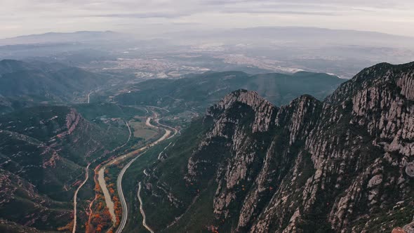 Aerial View on Serpentine Road with Riding Cars and Peaks of Montserrat Mountain Range Near