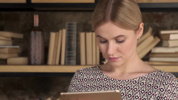 Good Looking Woman Using A Tablet near bookshelf. Beautiful girl touch computer