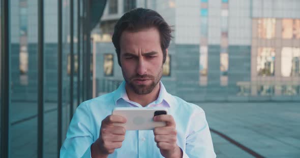 Bearded Man in Suit Playing on Smartphone in Game and Losing in Urban City Background