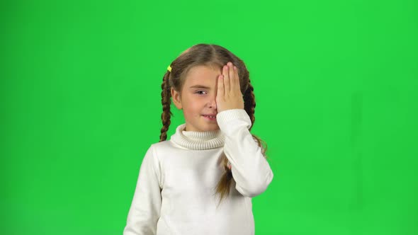 Little Female Is Hiding Face with Hands on Green Background.