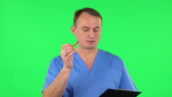 Medical Man Fills Papers at Black Folder with Pensil. Green Screen