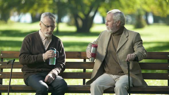 Old Men Enjoying Hot Tea From Thermo Cups, Siting on Bench Outdoor, Retirement