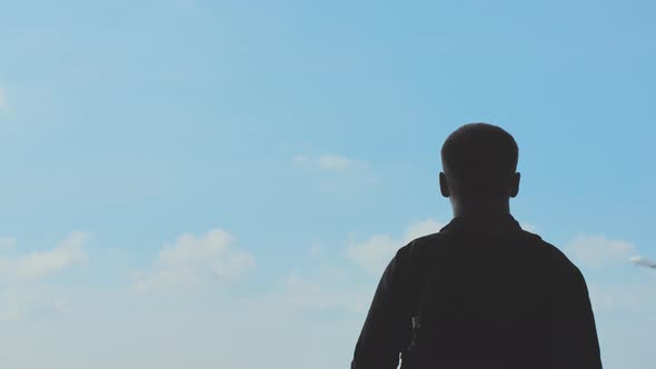 Silhouette of a Young Man Watching the Takeoff of an Airplane Against a Blue Sky