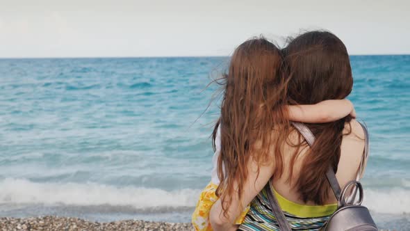 A Young Woman with Long Dark Hair Enjoys the View of the Azure Ocean with Her Little Daughter