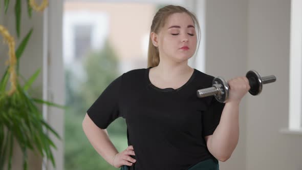 Middle Shot of Young Charming Plump Woman Exercising with Dumbbell at Home and Yawning