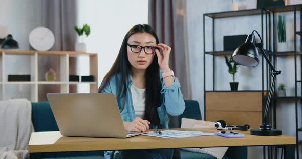 Asian Girl Taking off Eyeglasses when Looking Into Camera at Her Workplace