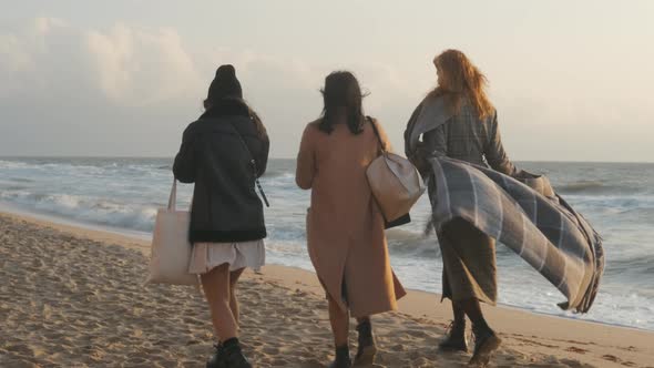 Three Beautiful Young Women Walking on the Sand Beach at Sunset or Sunrise